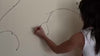 Video of woman painting branches on white wall.